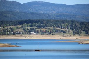 Une bateau flotte entre deux langues de terres qui s'étirent jour après jour dans le lac de Naussac.