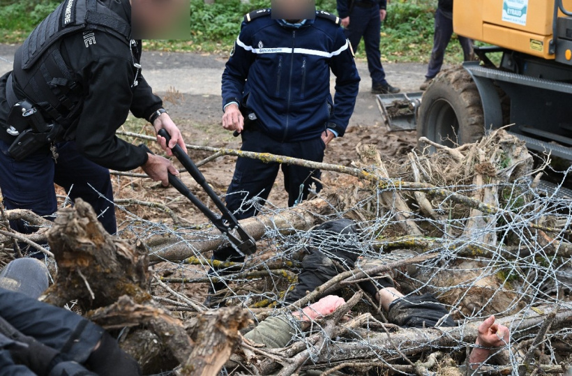 Un militant sous un amas de branches et de barbelés pour empêcher le passage de l'engin. 