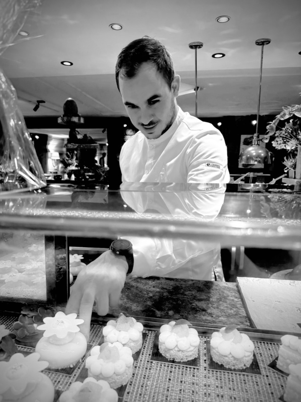 Guillaume Abrevoir devant une vitrine remplie de desserts qu'il a créés
