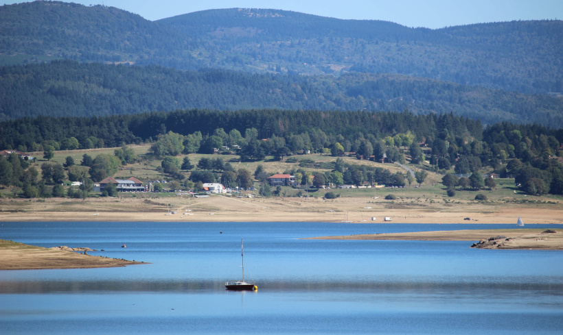 Une bateau flotte entre deux langues de terres qui s'étirent jour après jour dans le lac de Naussac.